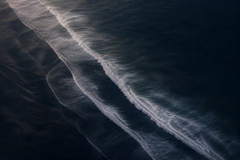Aerial long-exposure abstract of soft surf lines over deep ink-blue water